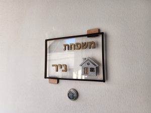 שלט דלת בעבודת יד עם רקע אקרילי שקוף, טקסט מעץ בצבע טבעי ועיצוב בית קטן מעץ.